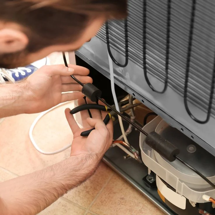 Technician checking wiring behind a refrigerator